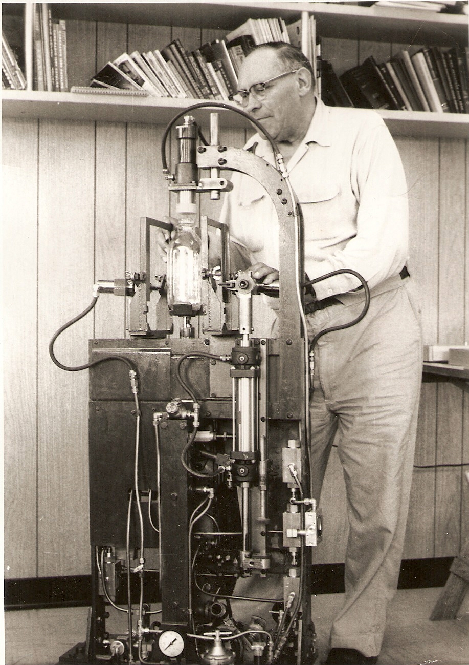 An early Strutz semi-automatic screen decorating machine with a glass bottle loaded in the carrier, being operated by hand